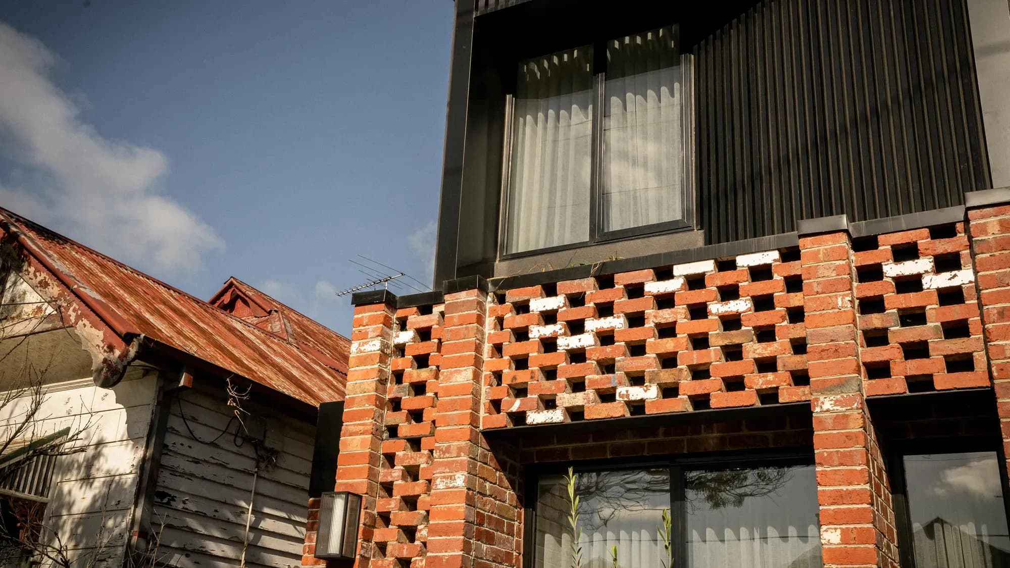 The dark-clad upper storey seen from the street, over perforated red brick