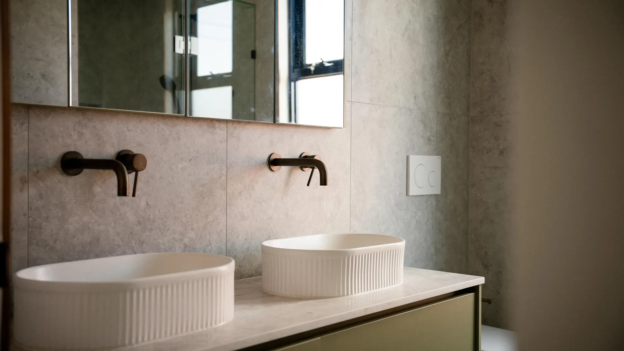 A bathroom with twin basins, black tapware and a wide mirror