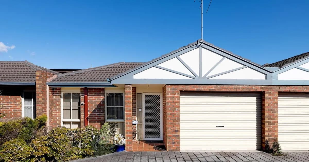 A brick villa unit with a white gabled porch under a clear sky