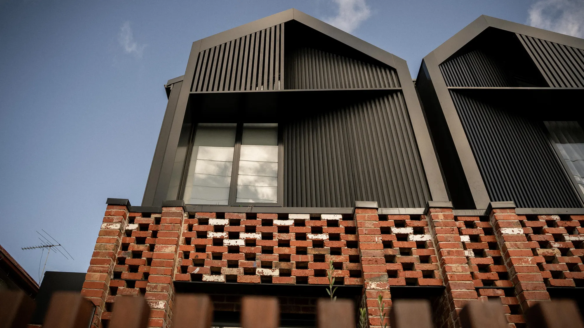 Twin dark-clad gables over a perforated red-brick ground floor