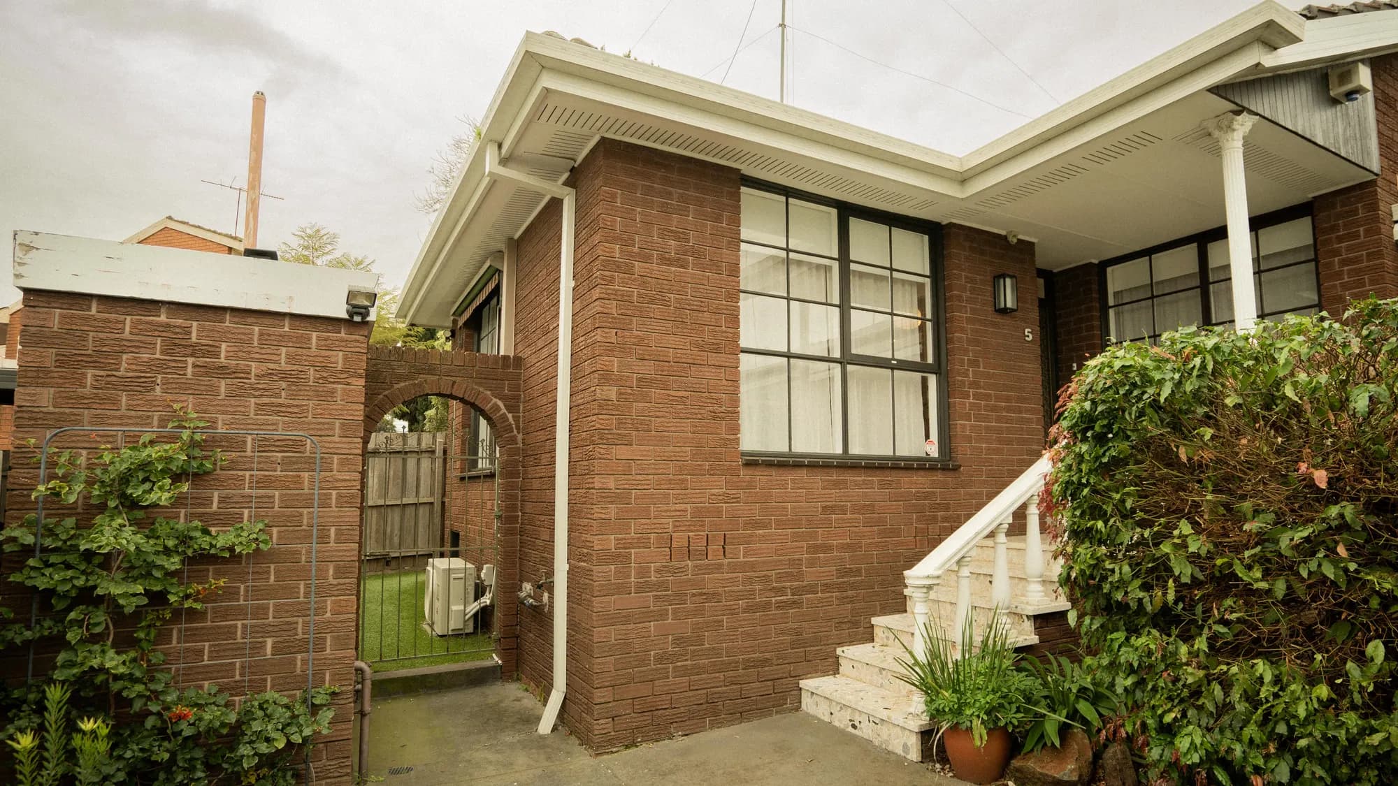 A red-brick unit behind an arched gateway and a clipped hedge