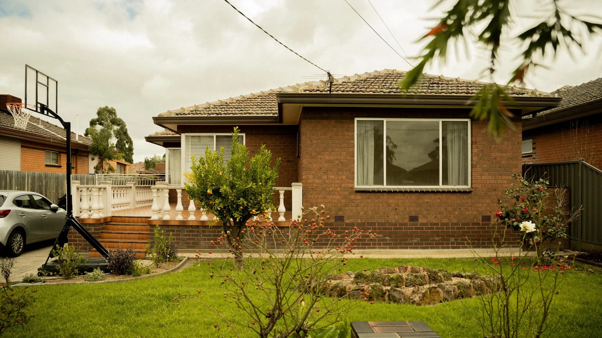 A red-brick home behind a white balustrade, a citrus tree on the front lawn