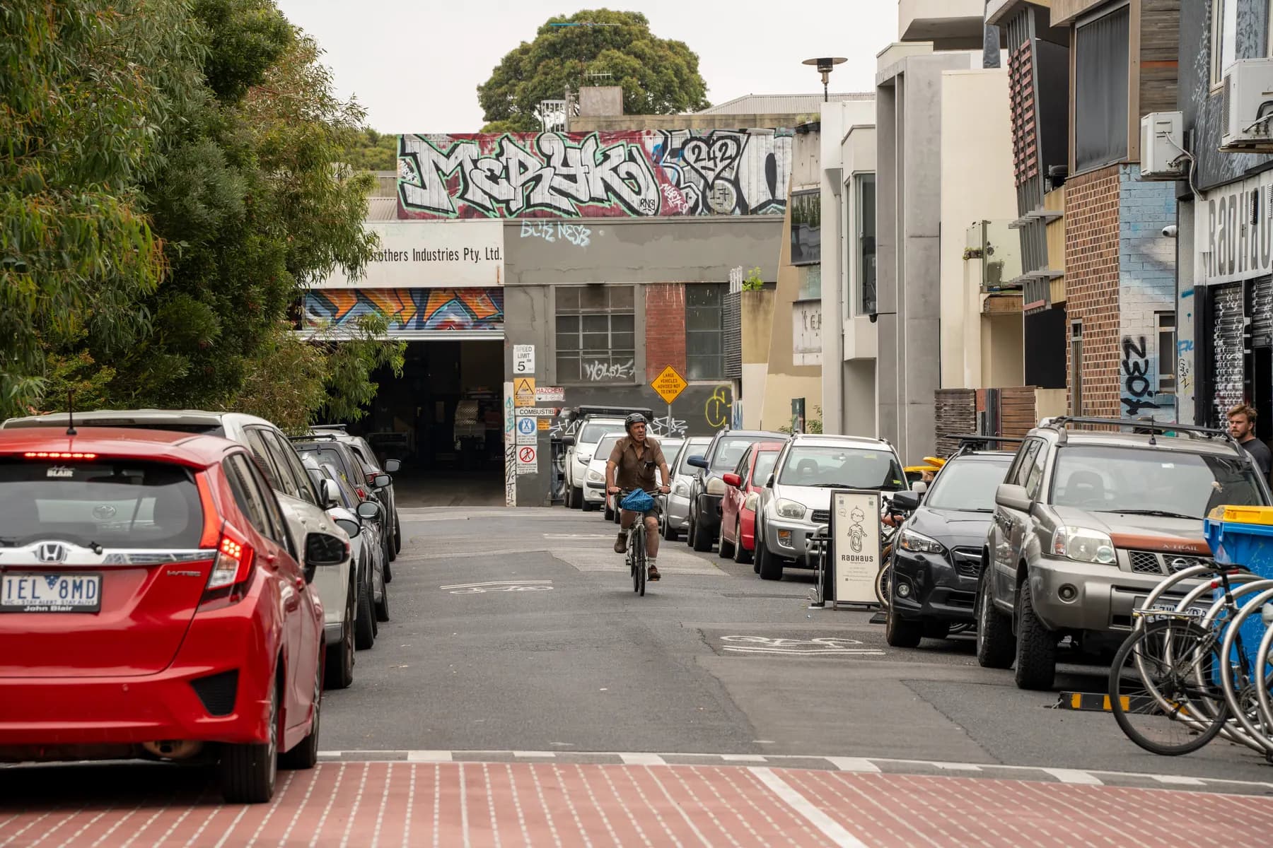 A cyclist riding up a graffitied Brunswick side street between parked cars