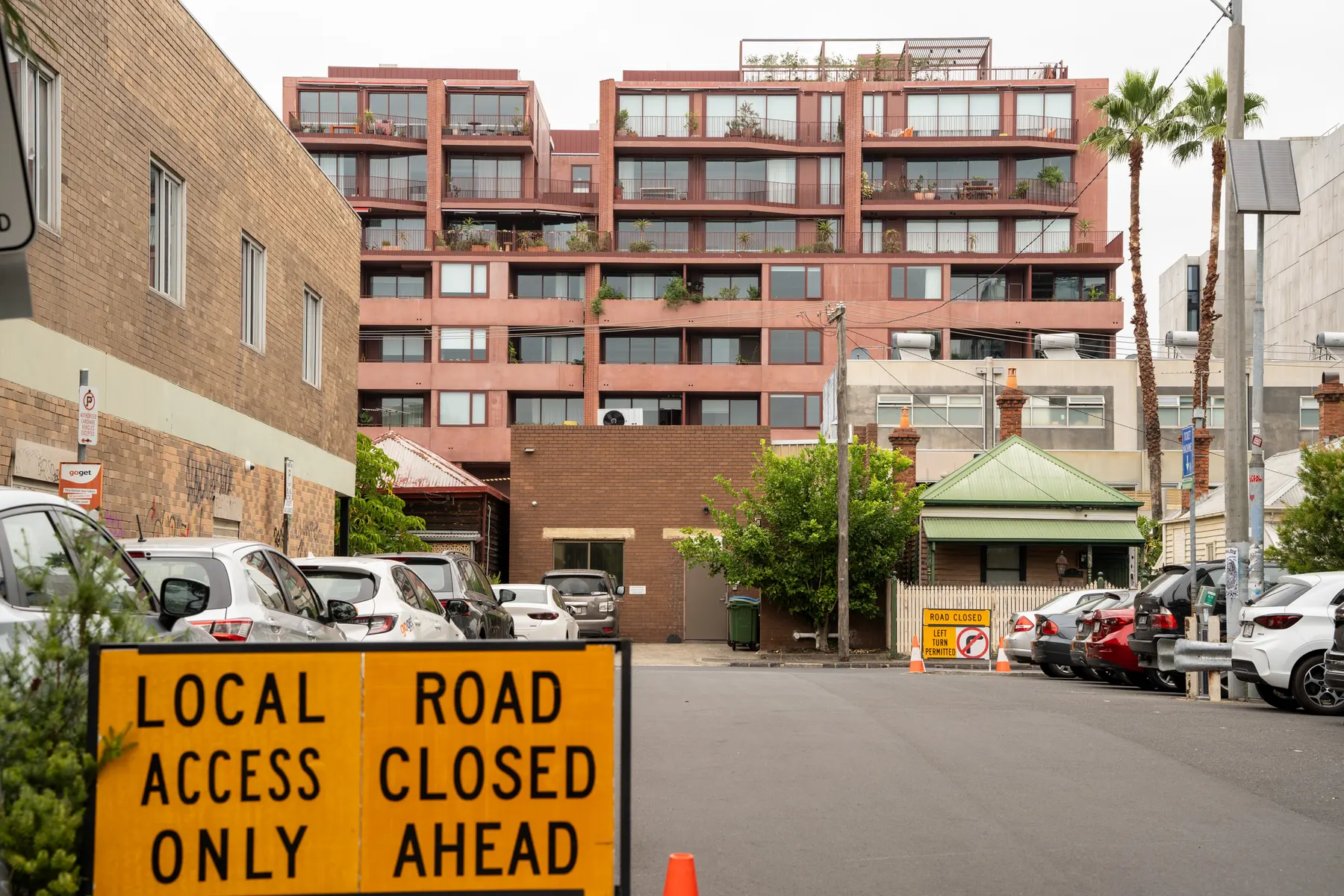 A new apartment building rising behind Victorian cottages and brick workshops