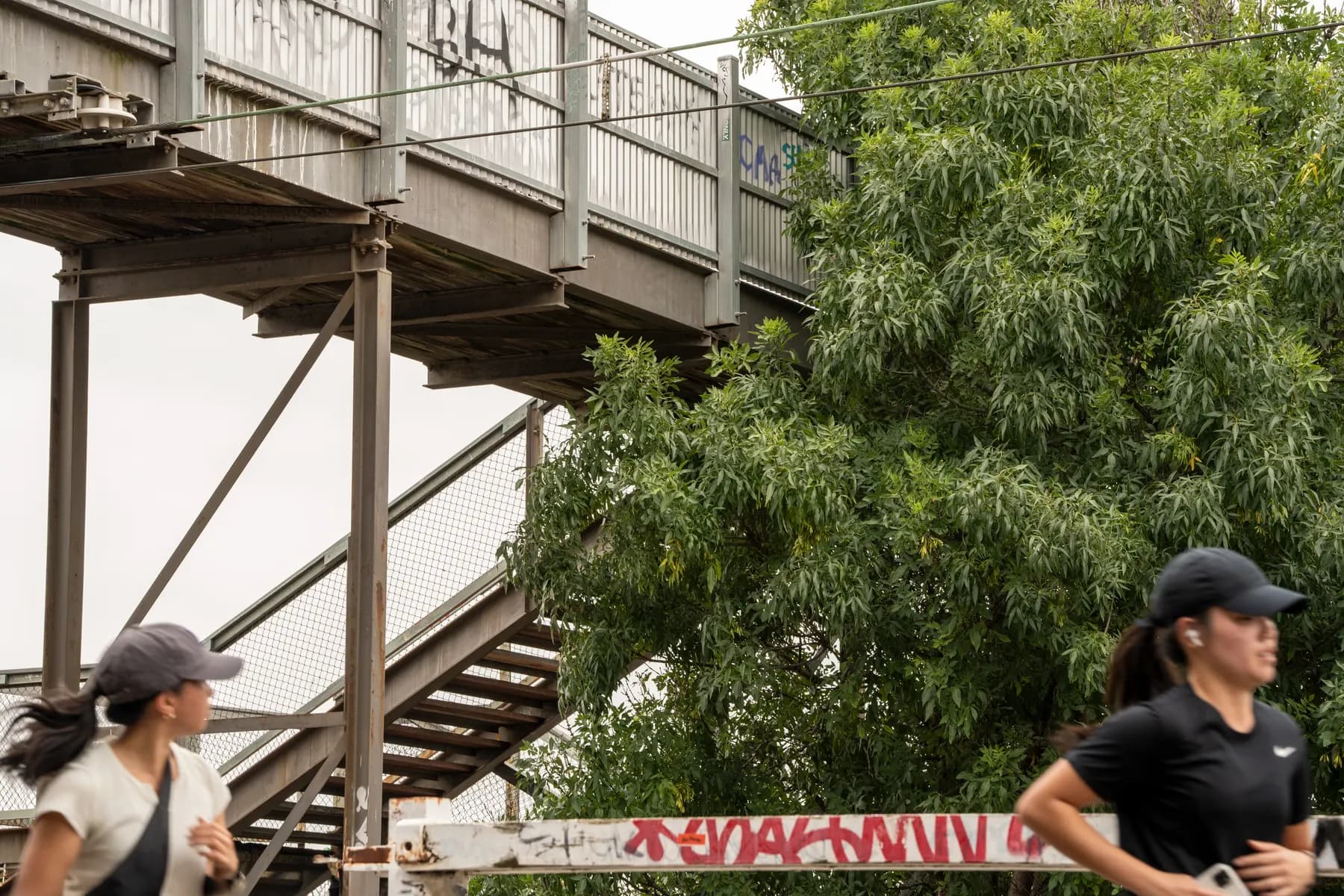 A pedestrian footbridge over the rail line, two runners passing beneath