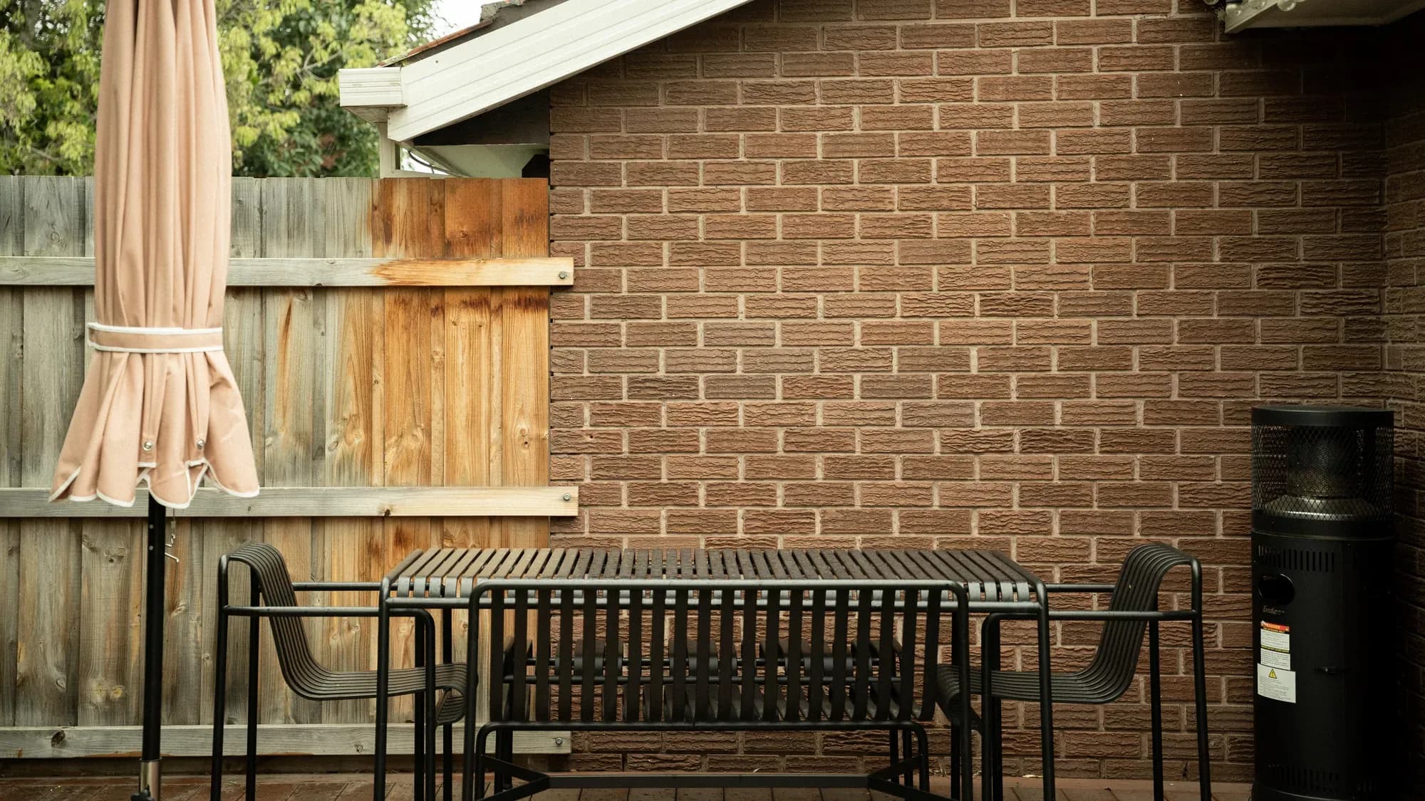 An outdoor table against the brick wall, paling fence behind