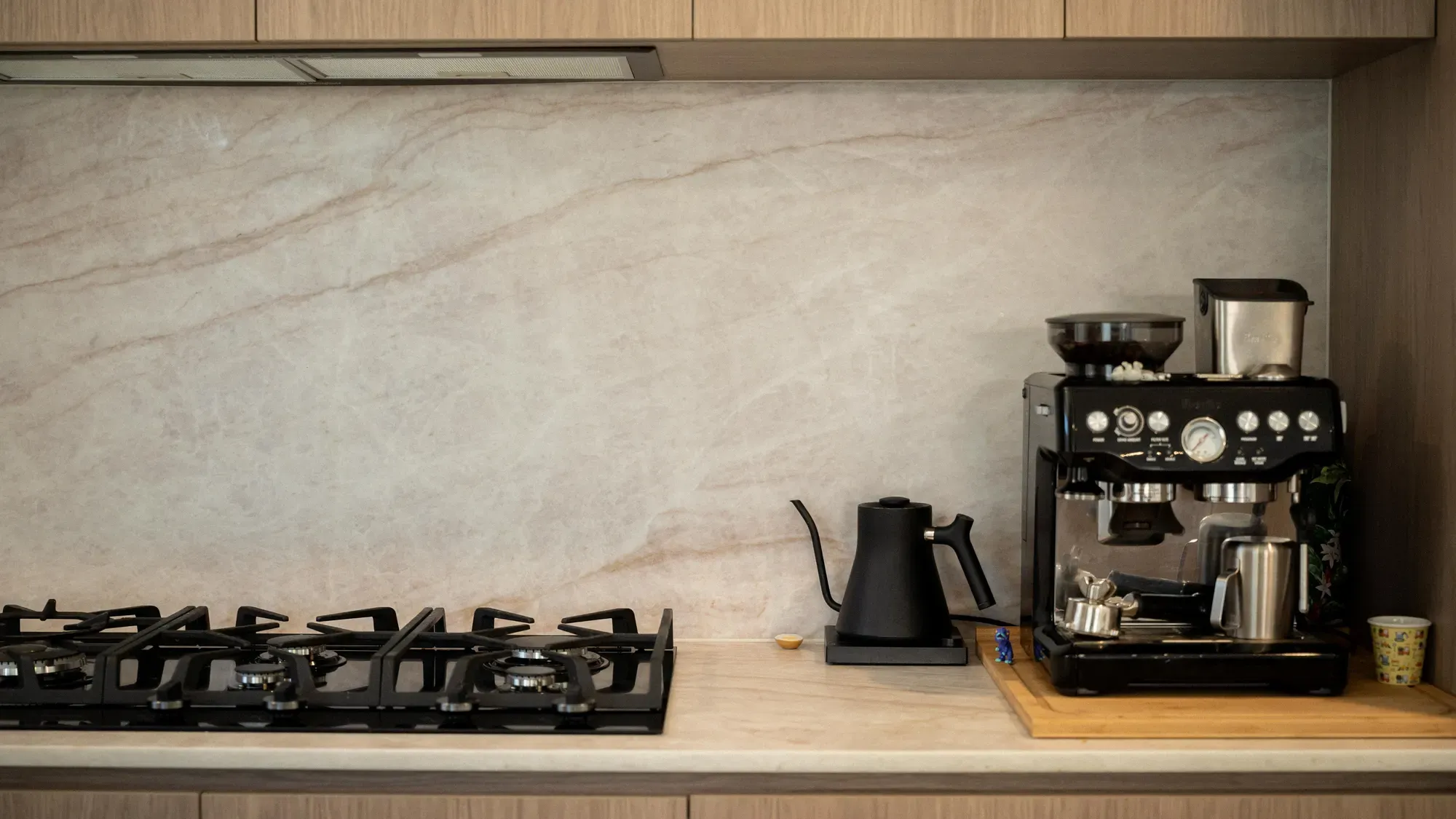 A stone splashback behind a gas hob, kettle and espresso machine